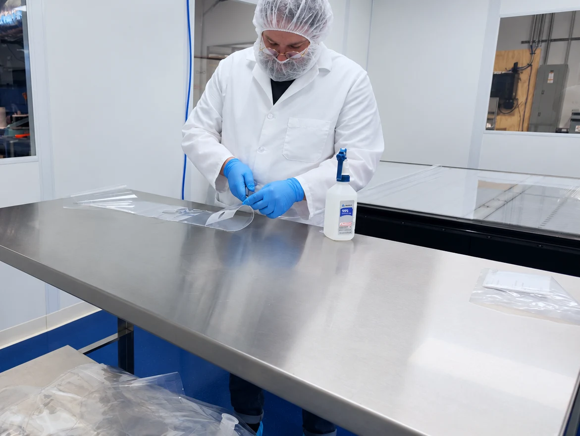 Technician in cleanroom gown, hairnet, beard cover and gloves assembling a single-use bag by hand in Alphinity's cleanroom